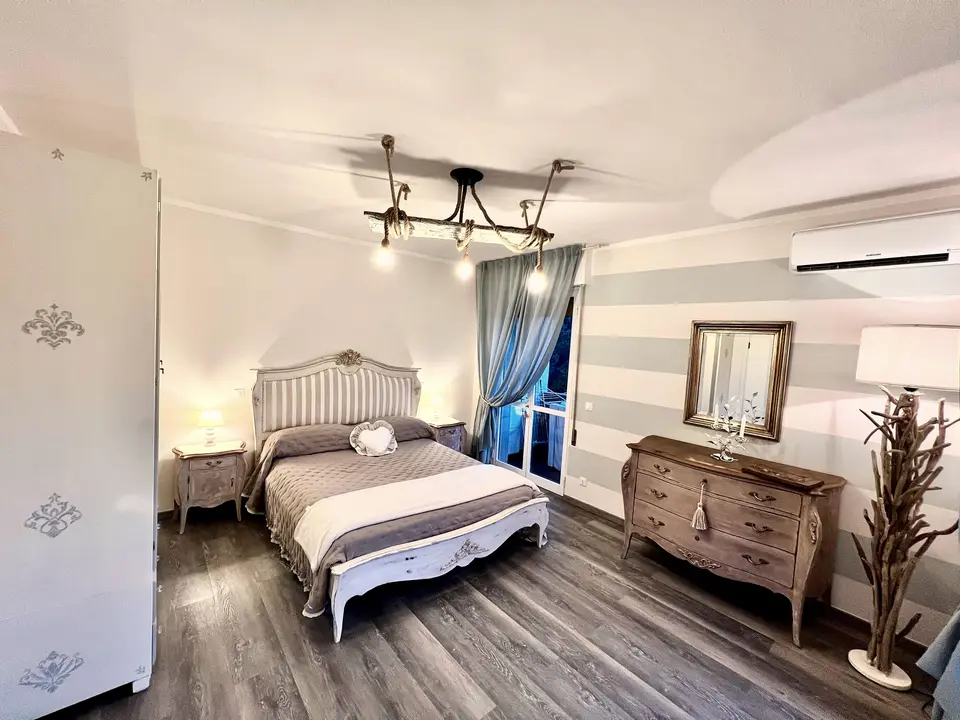 Camera matrimoniale della casa vacanze, con testiera a righe, armadio decapato e trave a vista con lampadine