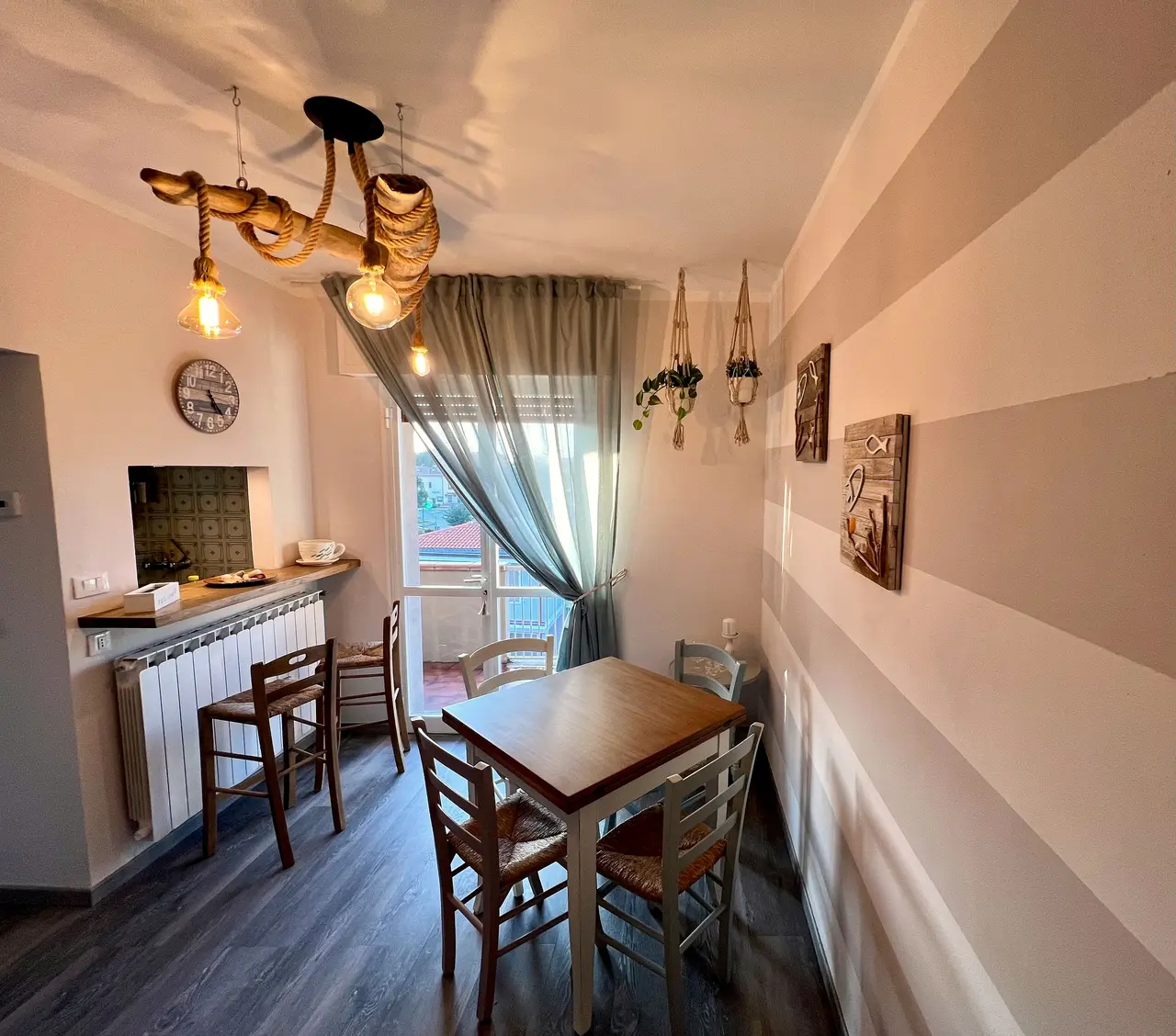 Zona pranzo con orologio di legno e sedie impagliate davanti alla porta-finestra socchiusa