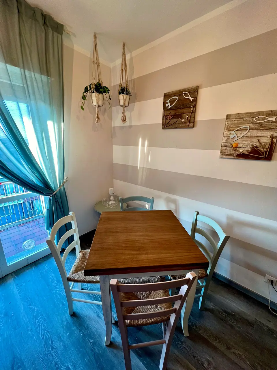 Tavolo da pranzo in legno chiaro davanti alla porta-finestra con tenda azzurra